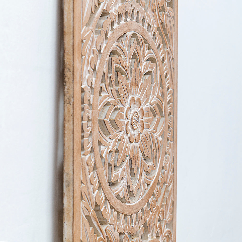 Close-up of a carved wooden wall panel with an intricate floral mandala design in a light natural wood finish against a plain white wall.