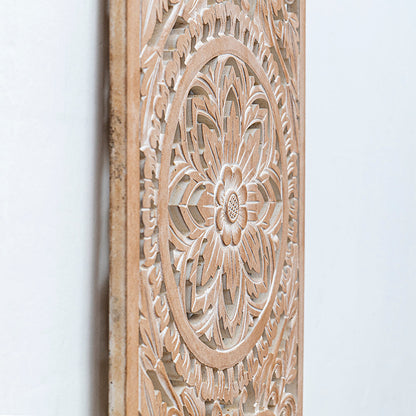 Close-up of a carved wooden wall panel with an intricate floral mandala design in a light natural wood finish against a plain white wall.