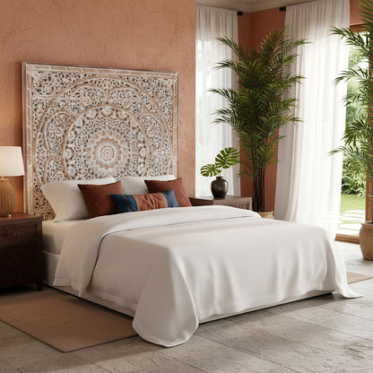 Decorative tapestry on a wall above a bed with pillows in a bright bedroom.